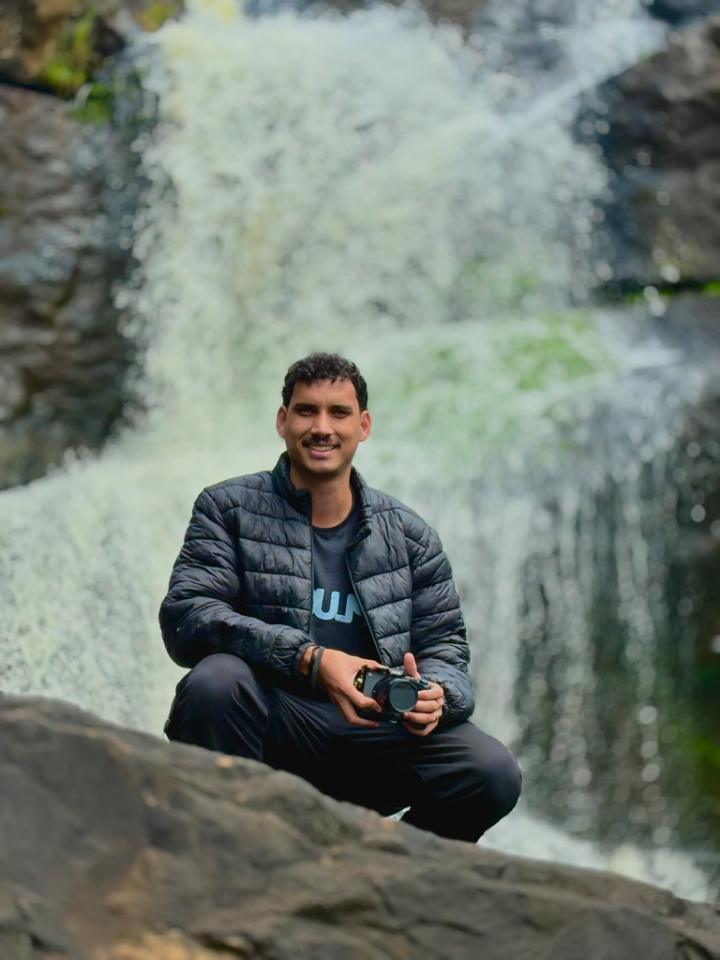Victor segurando uma câmera em frente a uma cachoeira